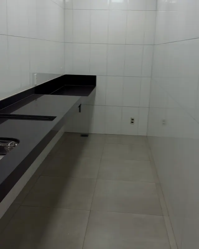 Cantina: bancada longa de granito preto com cuba de inox e paredes de azulejo branco.