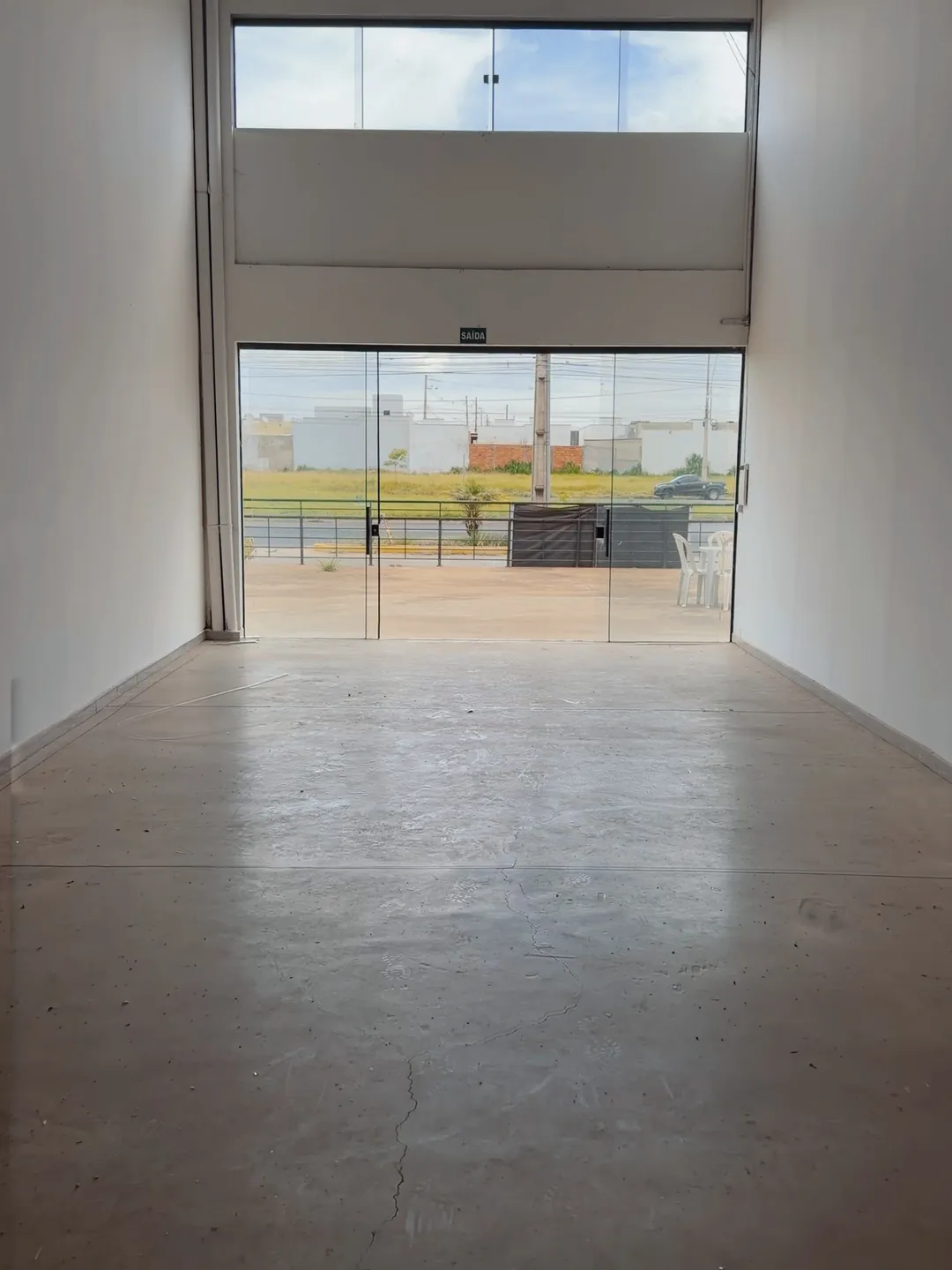 Foto com tratamento digital: interior vazio de uma loja do complexo, paredes brancas, piso de concreto limpo e a vitrine de vidro voltada para fora.