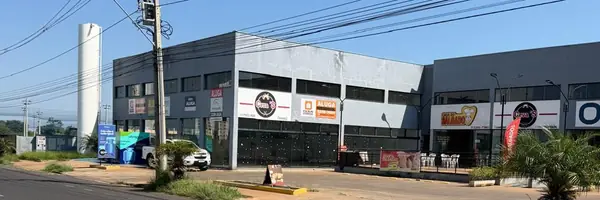 Salão das lojas 09 e 10 visto da Av. Aldo Borges Leão: bloco cinza de pé-direito alto com vitrines no térreo